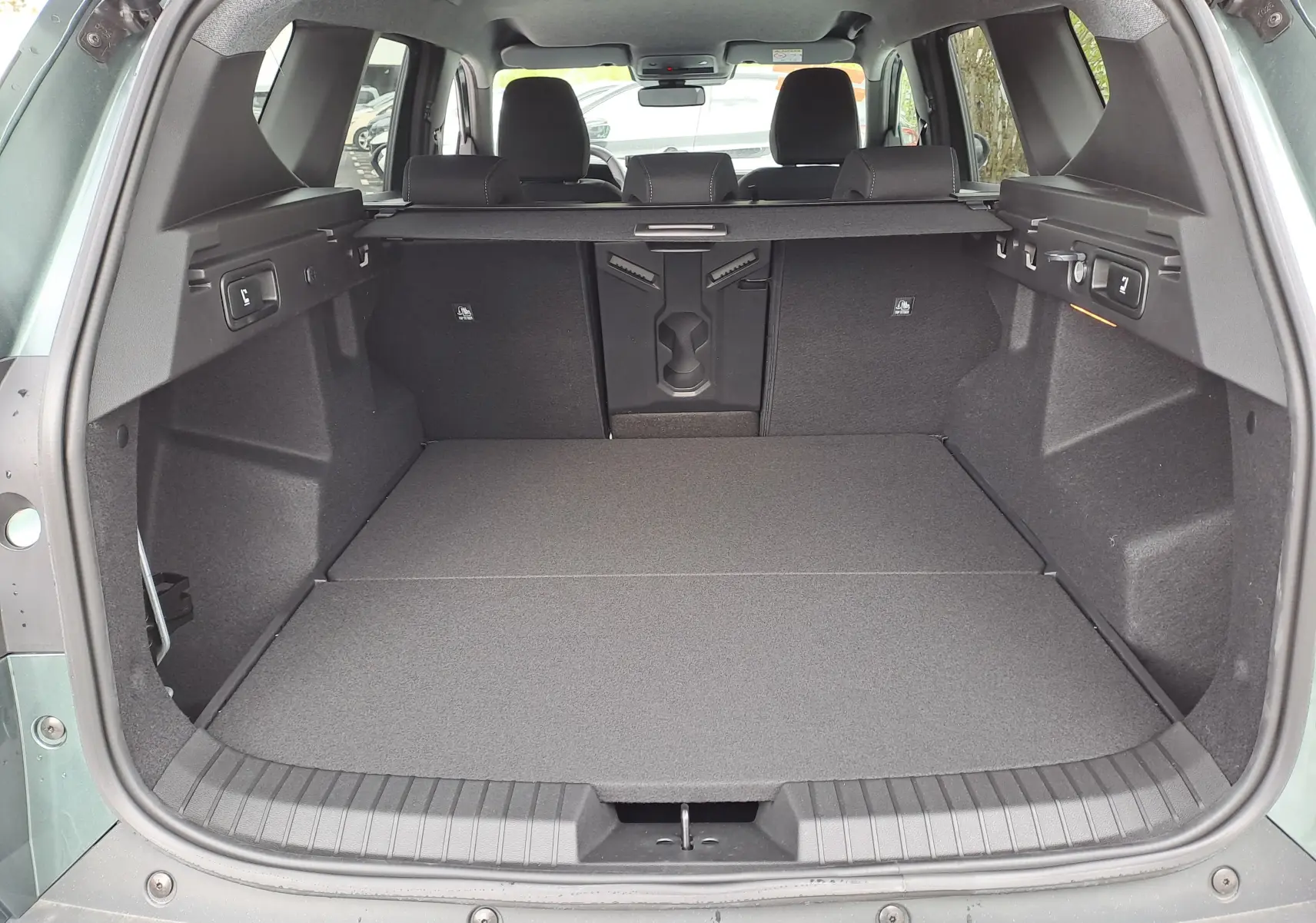 Coffre ouvert vu de l'arrière du Dacia Bigster vert cèdre, montrant un espace de chargement plat et bien aménagé.