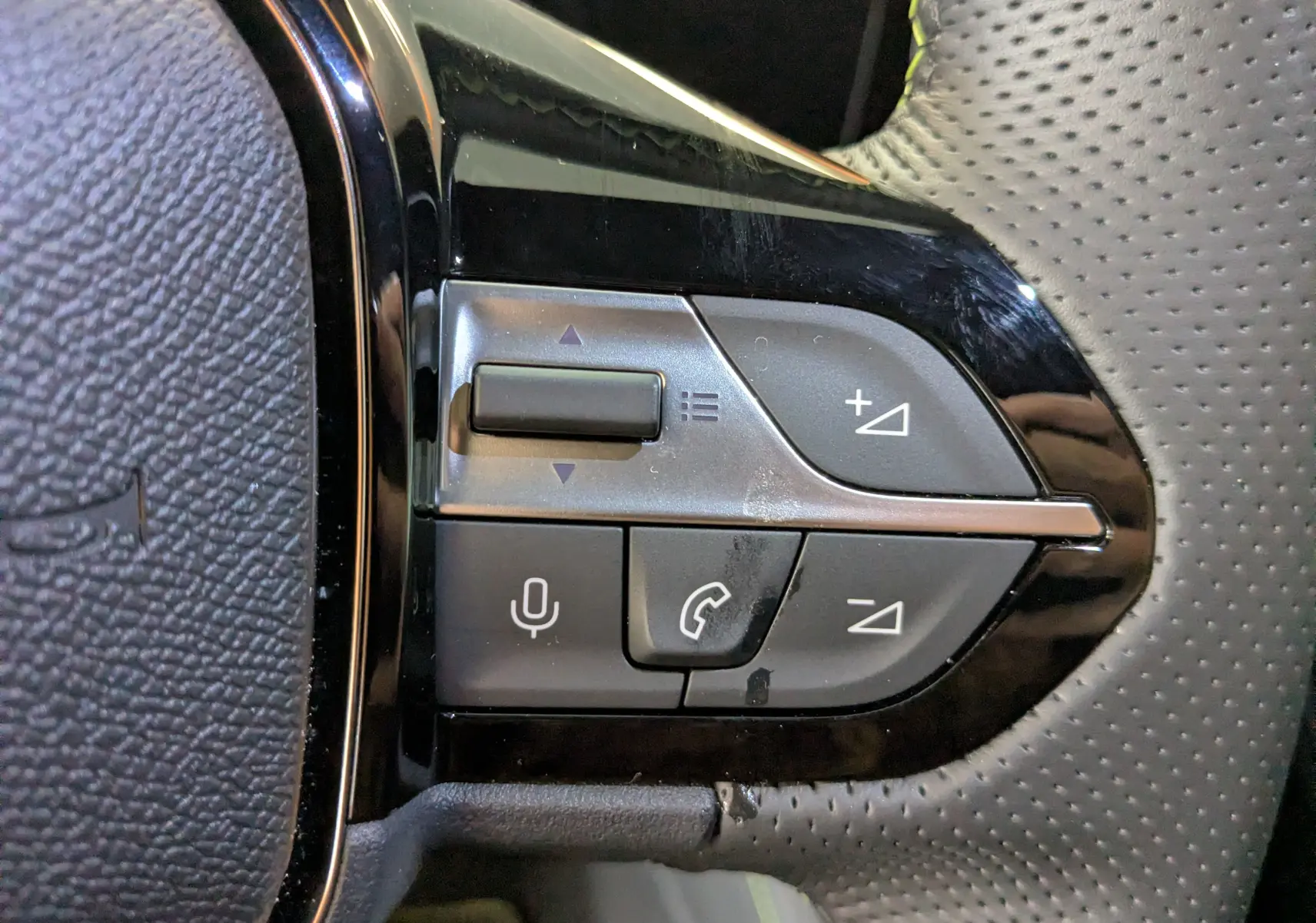 Gros plan sur les commandes au volant côté gauche du Peugeot 408 Hybrid 145 e-DCS6 GT, finition noire et perforée.