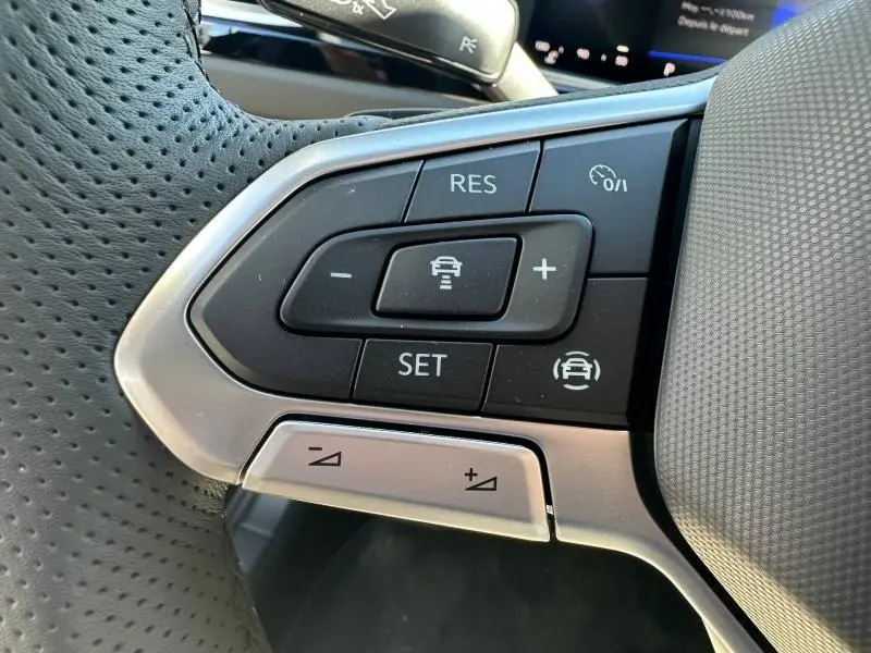 Gros plan sur les commandes du volant cuir perforé du Volkswagen T-Roc noir nacré, boutons de régulateur de vitesse et assistance conduite.