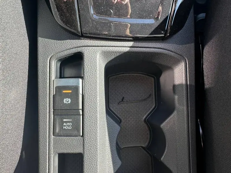 Vue rapprochée de la console centrale noire du Volkswagen T-Roc 2025, avec frein à main électrique et porte-gobelets.