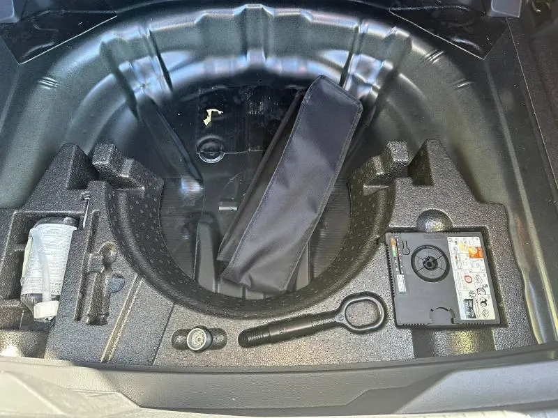 Vue plongeante sur le rangement sous coffre du Volkswagen T-Roc noir intense nacré, avec kit de réparation pneu et outils intégrés.