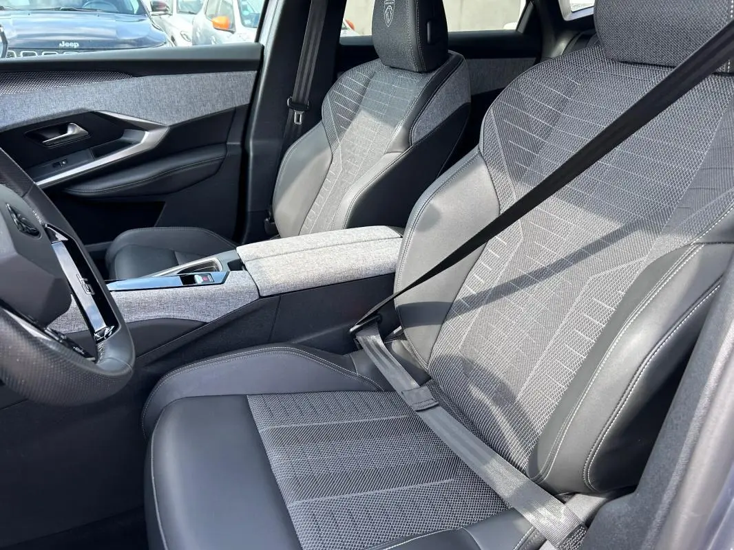 Vue intérieure côté conducteur du Peugeot 3008 Hybrid 136 e-DCS6 GT 2025, sièges gris clair avec cuir et tissu, accoudoir central.