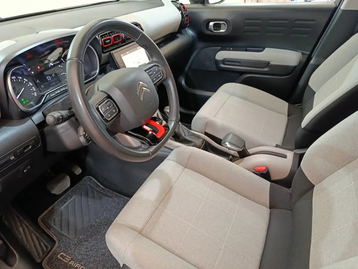 Vue intérieure côté conducteur de la Citroën C3 Aircross beige, avec volant cuir et sièges tissu clair à motifs carrés.