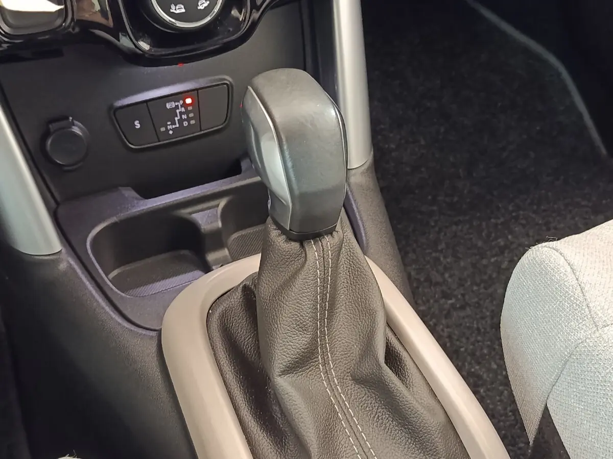 Le levier de vitesse automatique noir avec soufflet cuir beige clair, console centrale et siège tissu clair partiel visible.