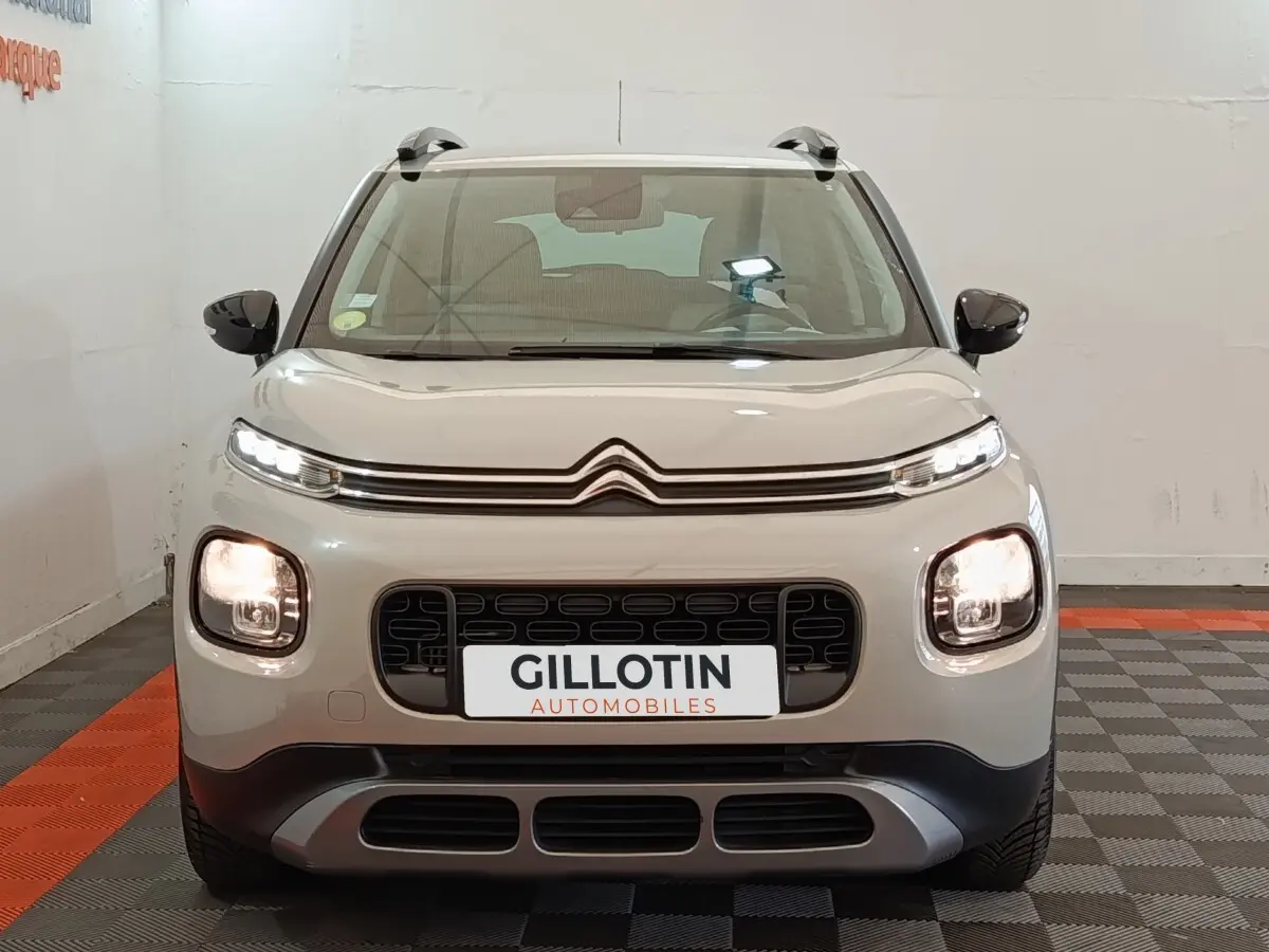 Citroën C3 Aircross beige vue de face, avec calandre noire et feux avant allumés en intérieur showroom.