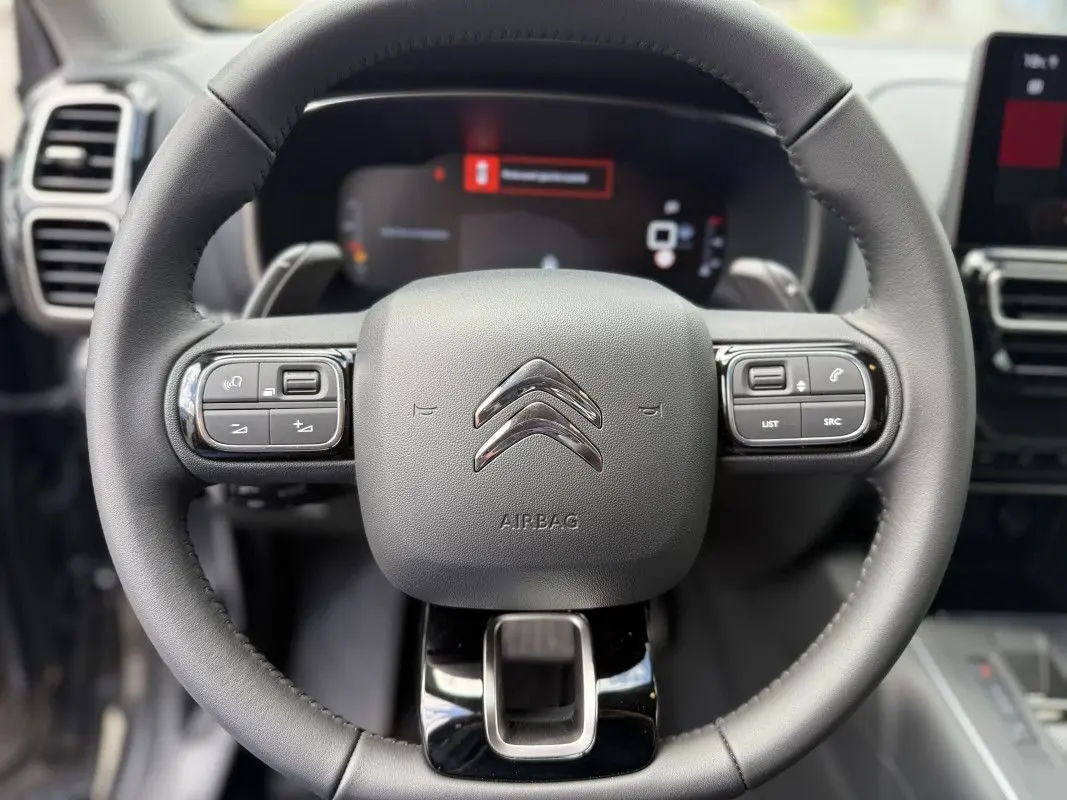 Vue rapprochée du volant en cuir noir du Citroën C5 Aircross 2025, avec commandes intégrées et logo chromé central.