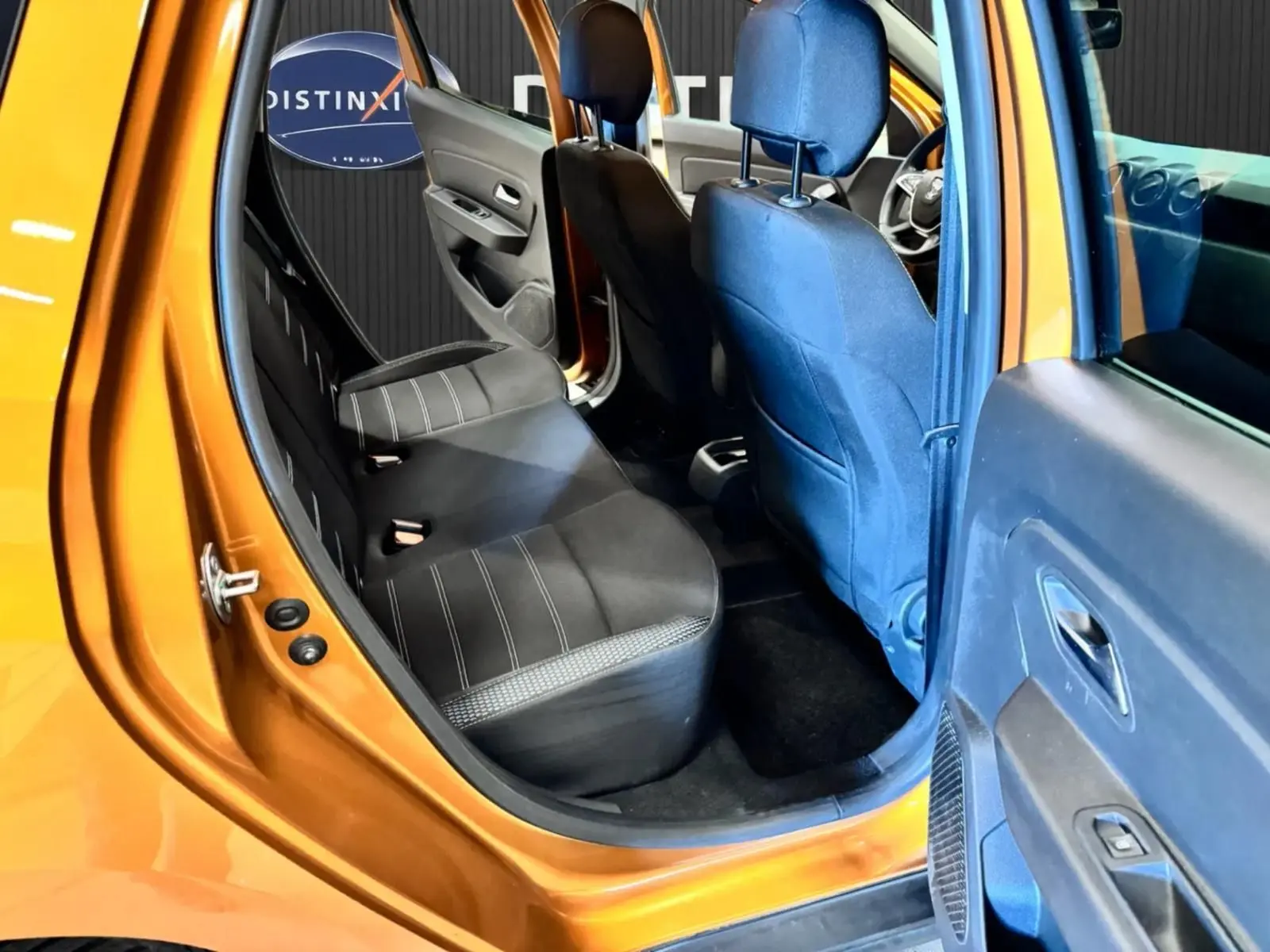 Vue intérieure côté gauche arrière du Dacia Duster orange 2020, montrant les sièges noirs et la porte ouverte.