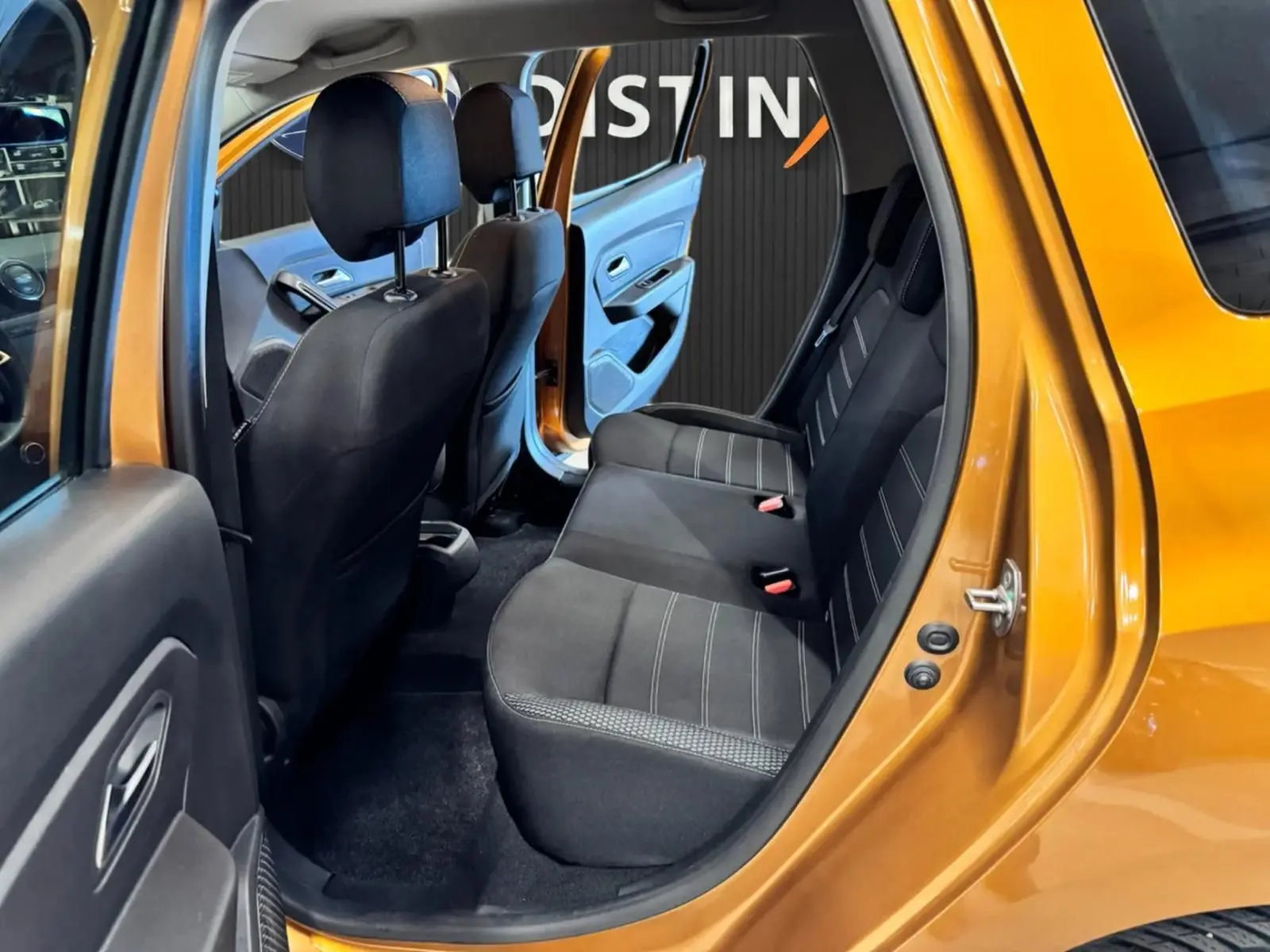 Vue intérieure côté gauche arrière du Dacia Duster orange 2020, montrant les sièges arrière en tissu noir avec surpiqûres grises.