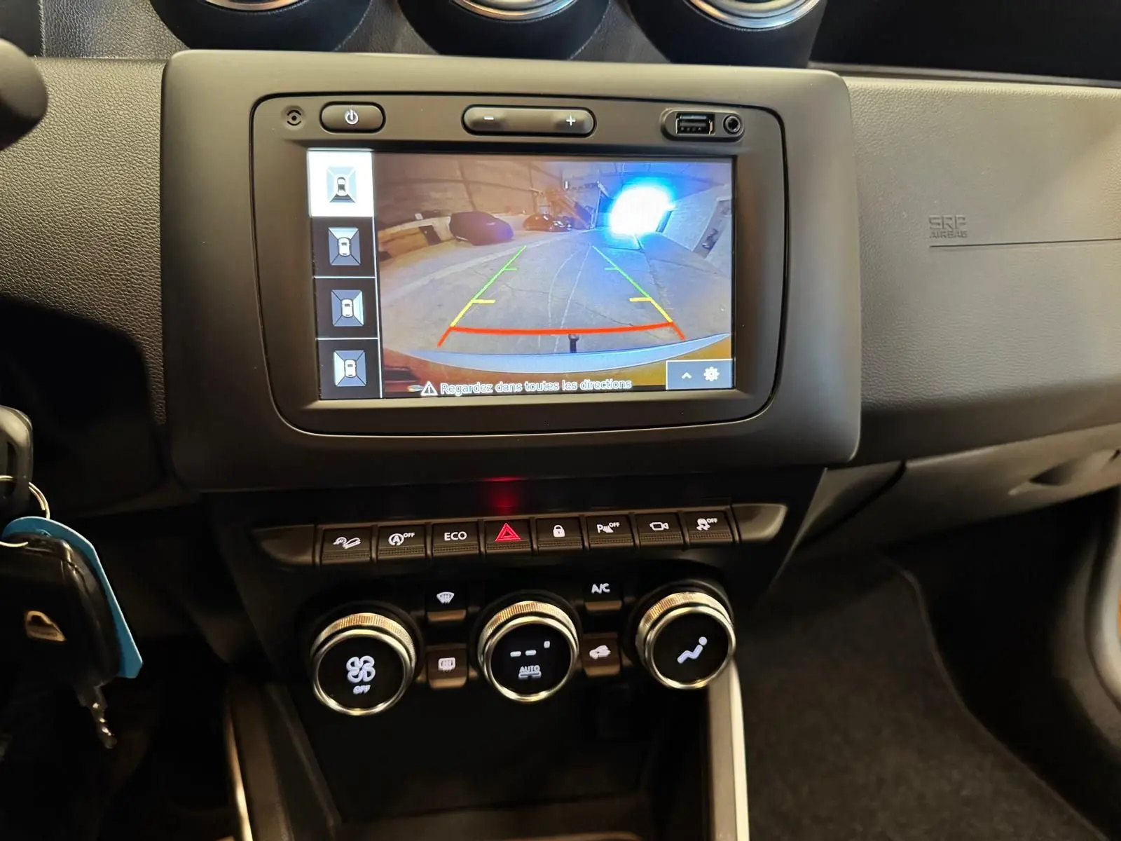 Vue rapprochée du tableau de bord du Dacia Duster 2020 montrant l'écran de caméra de recul et les commandes de climatisation.