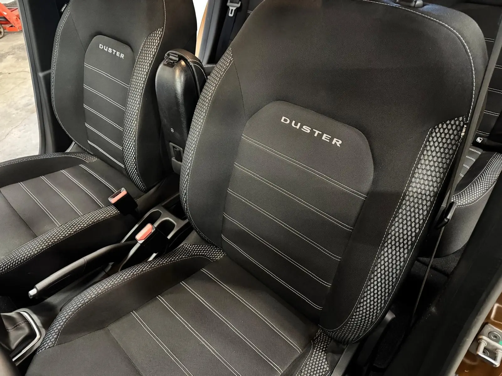 Vue rapprochée des sièges avant noirs du Dacia Duster avec logo DUSTER brodé et console centrale visible.