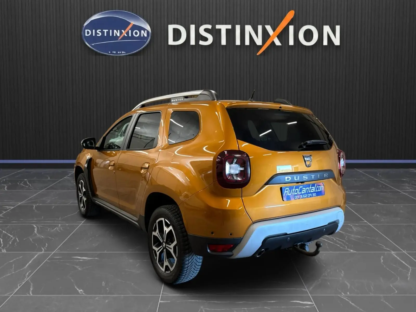 Vue 3/4 arrière droite d'un Dacia Duster orange 2020 avec attelage et jantes bi-ton dans un showroom.