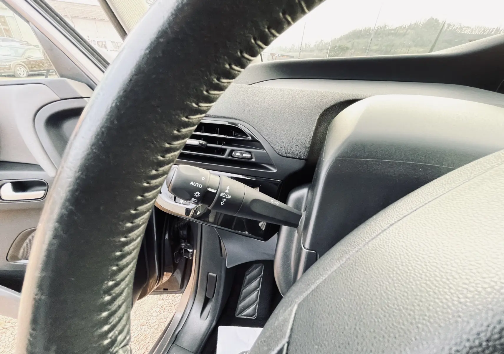 Gros plan sur la colonne de direction et le commodo d'éclairage à gauche du volant dans l'habitacle d'une Citroën C4 Picasso gris.