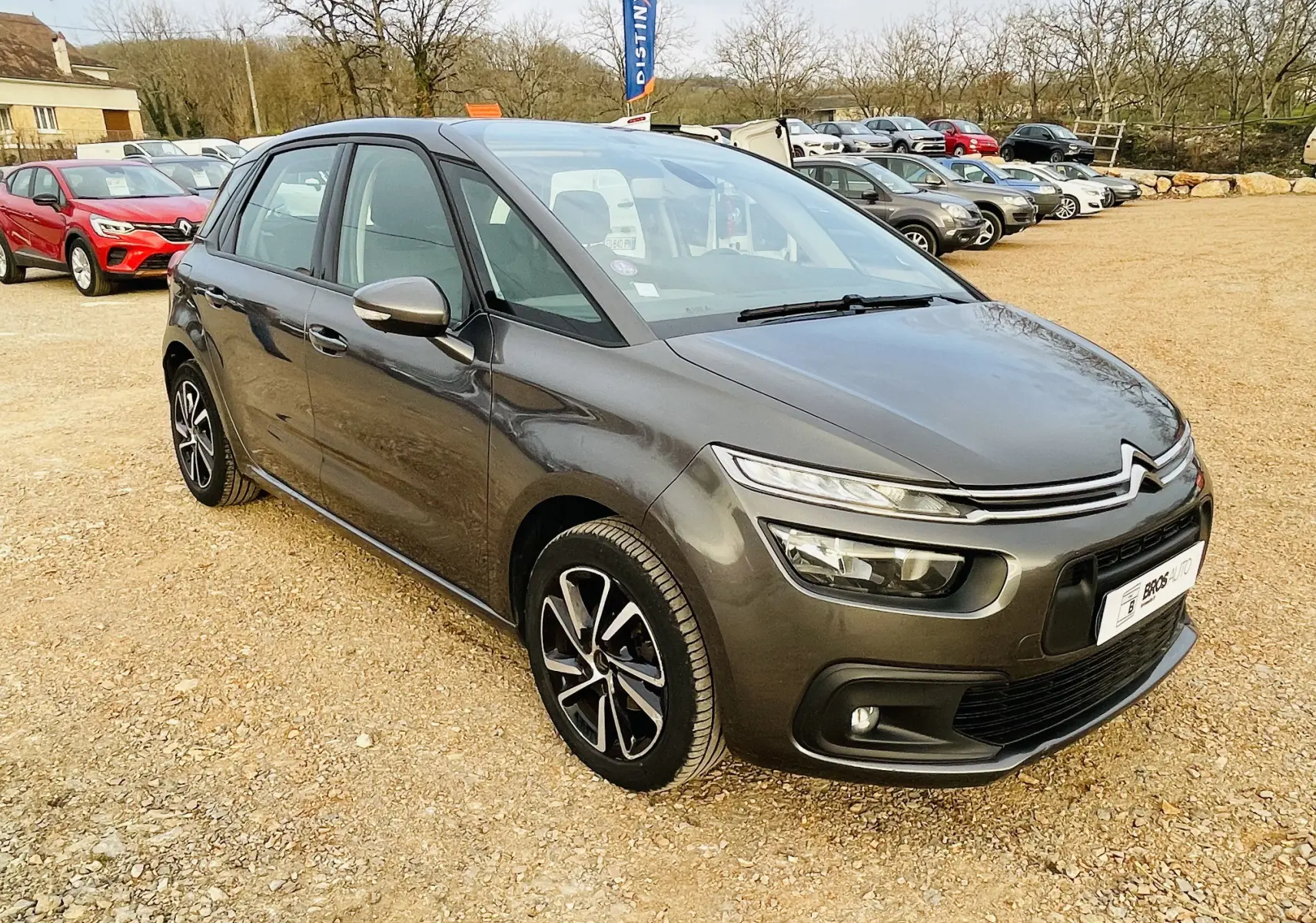 Citroën C4 Picasso II gris métal vue 3/4 avant droit sur parking avec jantes alliage noires et grises.