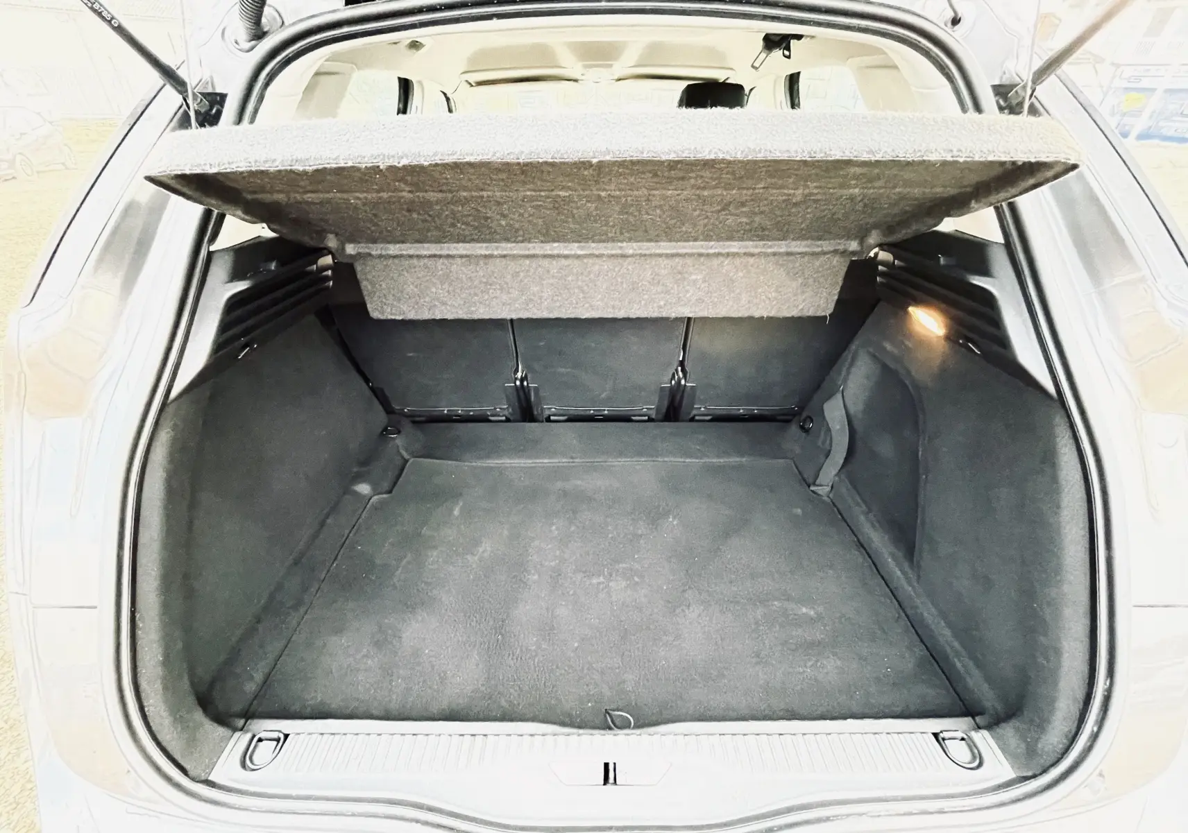 Coffre ouvert d'une Citroën C4 Picasso gris, vue arrière montrant l'espace de chargement et la tablette cache-bagages relevée.