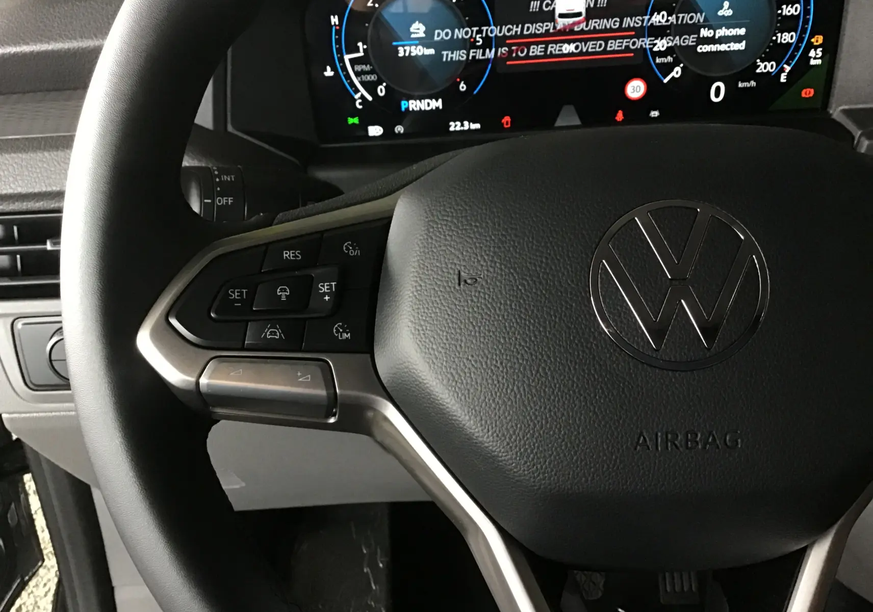 Gros plan sur le volant multifonction noir du Volkswagen Transporter T7 avec tableau de bord numérique en arrière-plan.