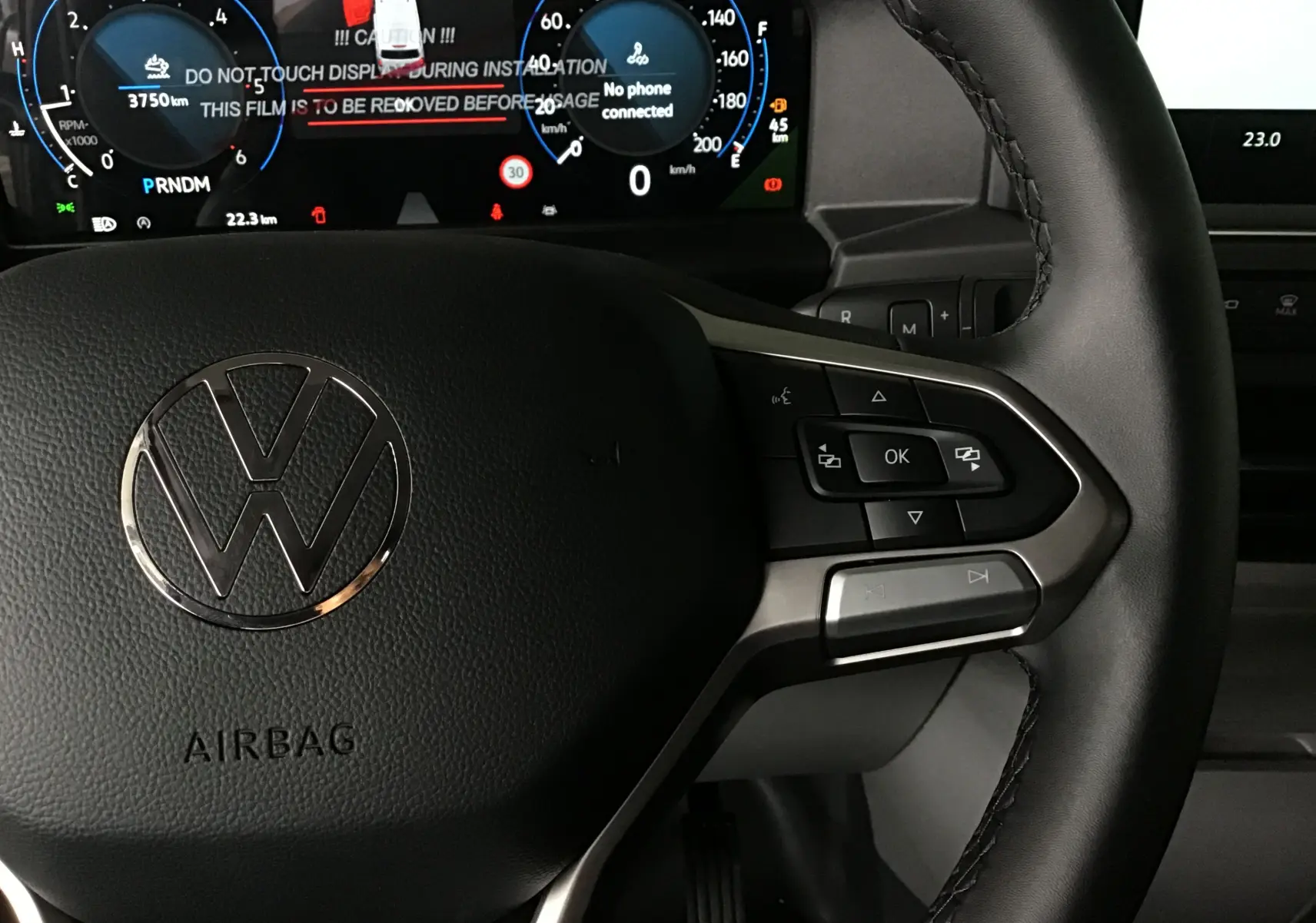 Vue rapprochée du volant cuir du Volkswagen Transporter T7 avec commandes multifonctions et tableau de bord numérique allumé.