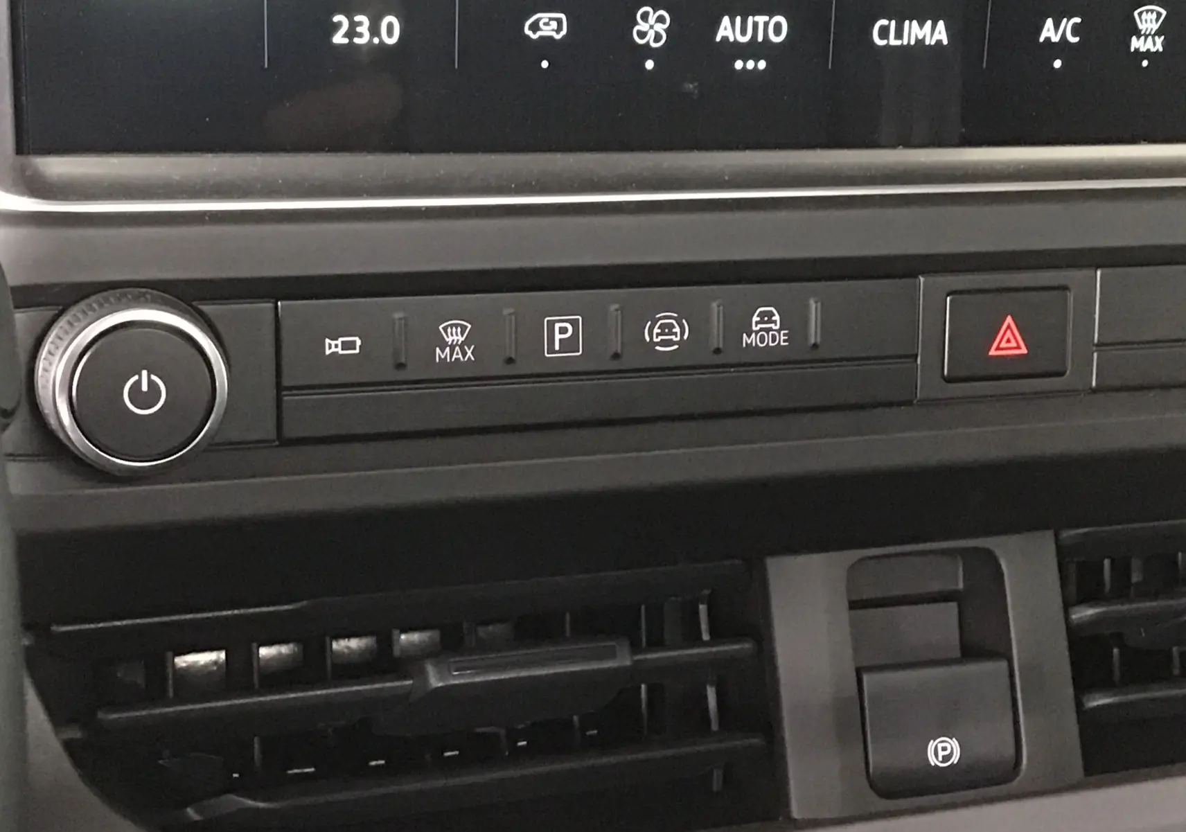 Gros plan sur la console centrale du Volkswagen Transporter T7, montrant les commandes de climatisation et le frein à main électrique.