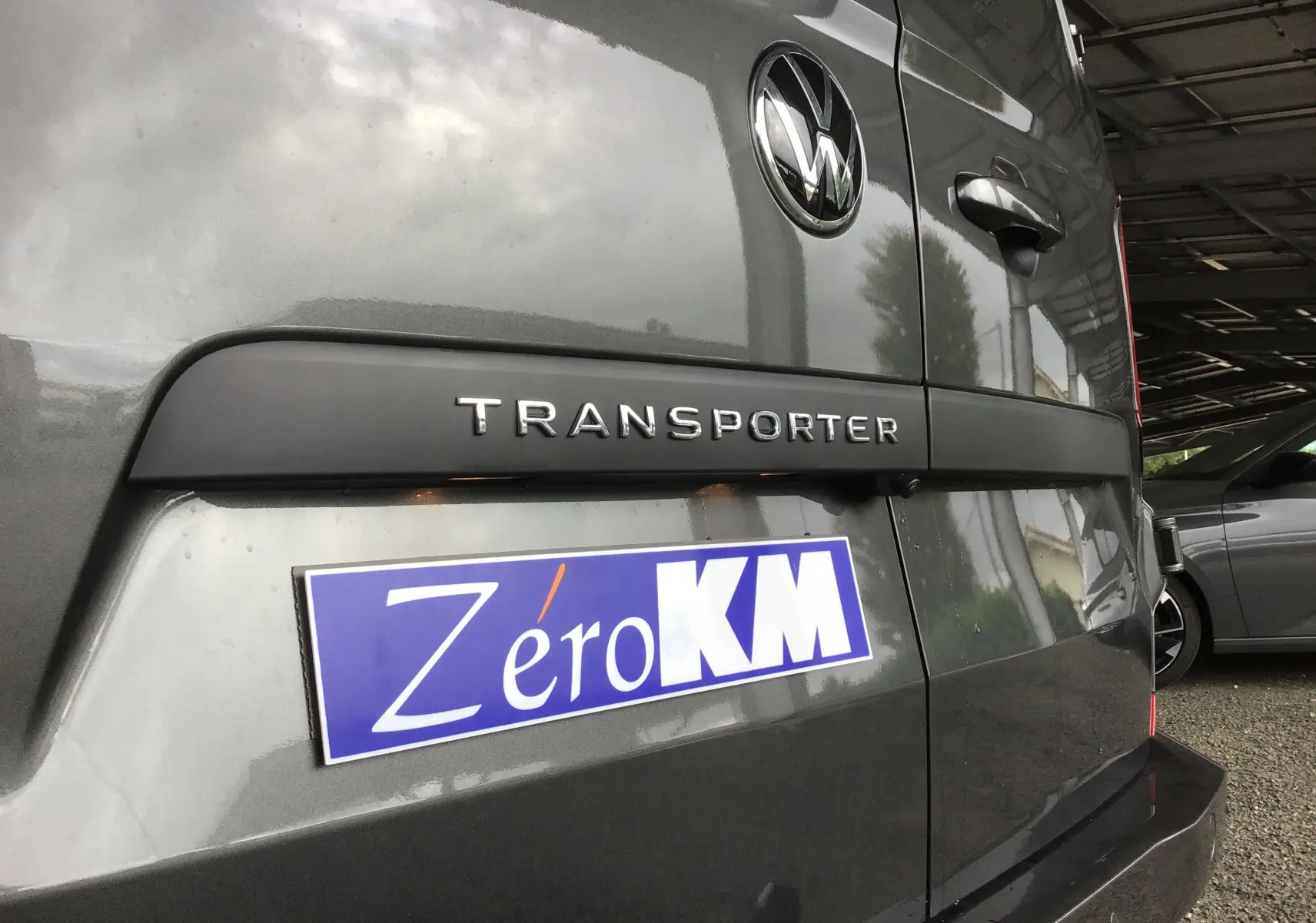 Vue rapprochée arrière droite du Volkswagen Transporter gris anthracite avec logo et plaque Zéro KM visible.