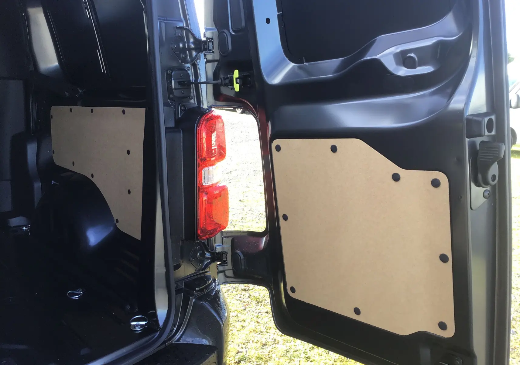 Vue intérieure de la porte arrière droite ouverte d'un Citroën Jumpy XL gris titane, montrant le panneau de protection en bois.
