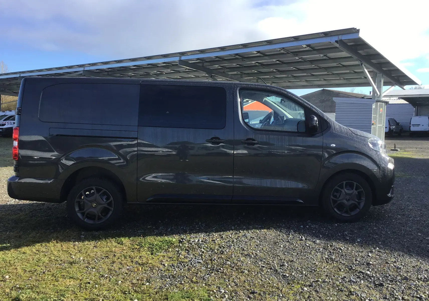Profil côté gauche d'un Citroën Jumpy cabine approfondie gris titane stationné sous un abri métallique.