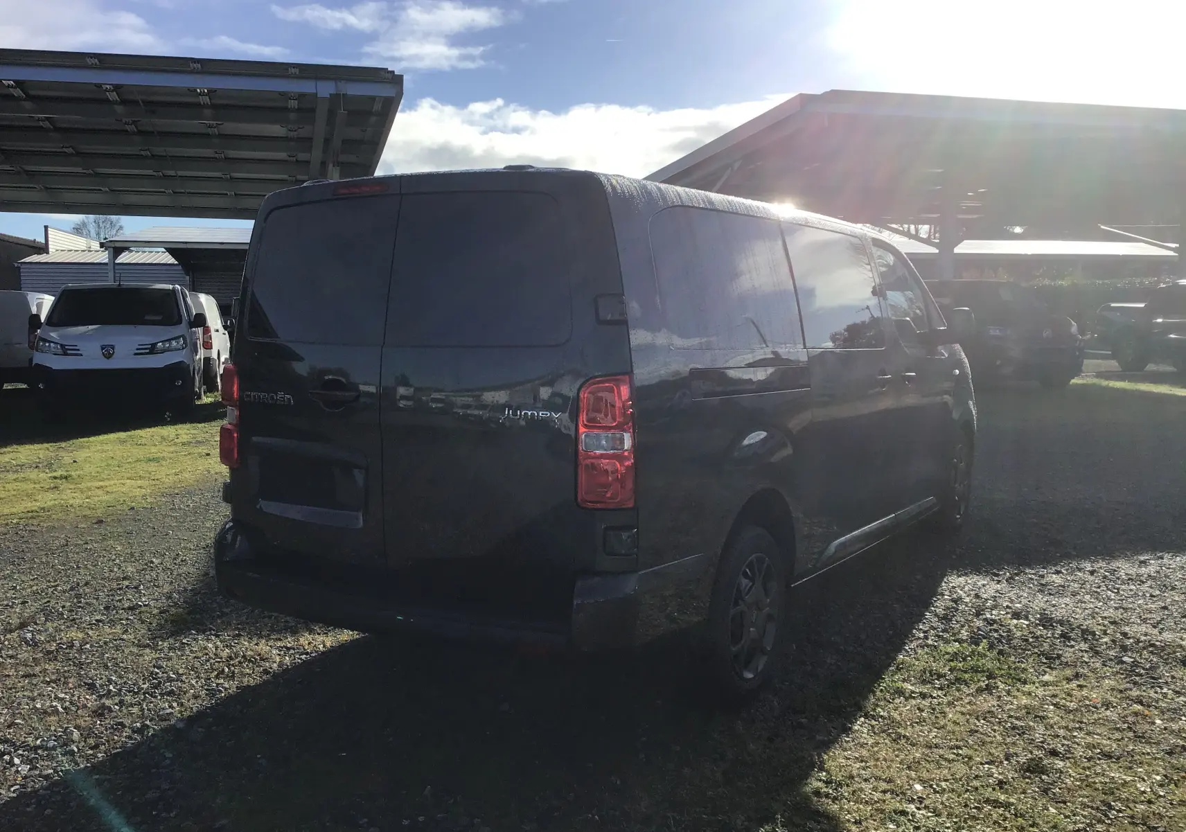 Vue 3/4 arrière d'un Citroën Jumpy cabine approfondie gris titane stationné sur un sol gravillonné en extérieur.