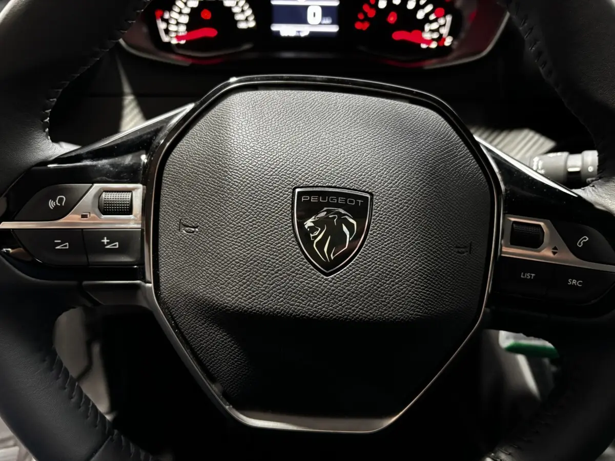 Gros plan sur le volant cuir noir du Peugeot 208 PureTech 100 S&S Active 2024 avec logo lion central et commandes intégrées.