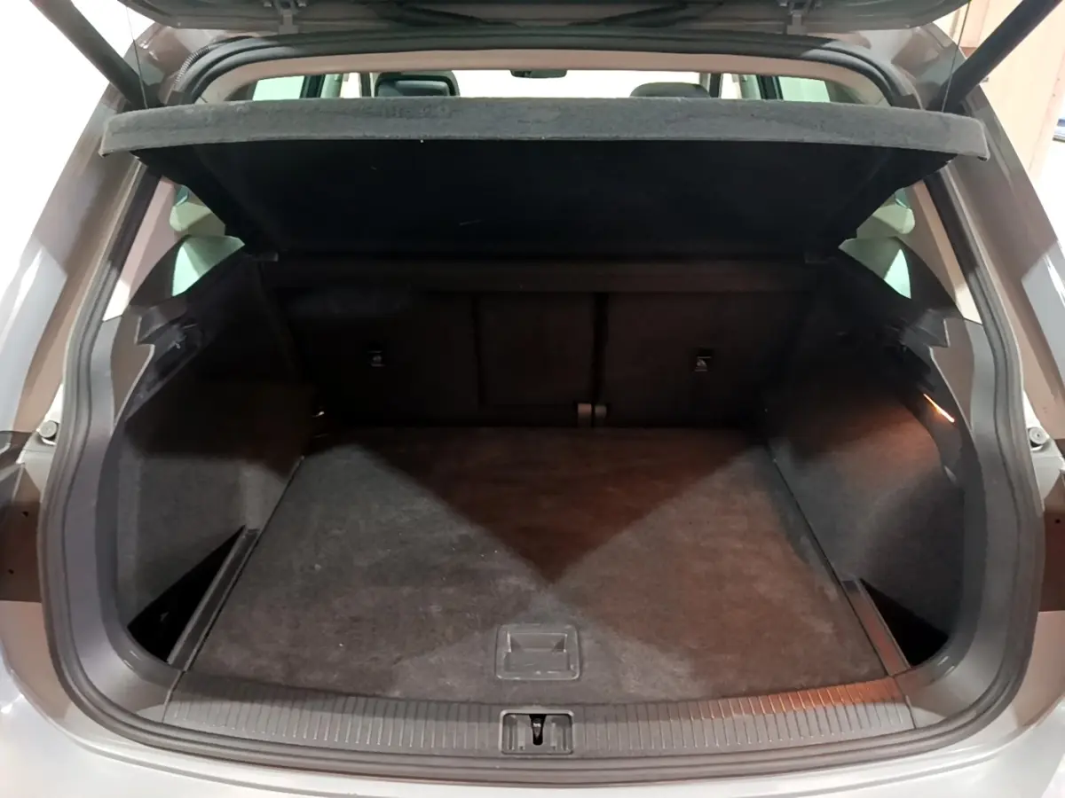 Coffre ouvert d’un Volkswagen Tiguan gris foncé, vue arrière montrant l’espace de chargement vide et la tablette relevée.