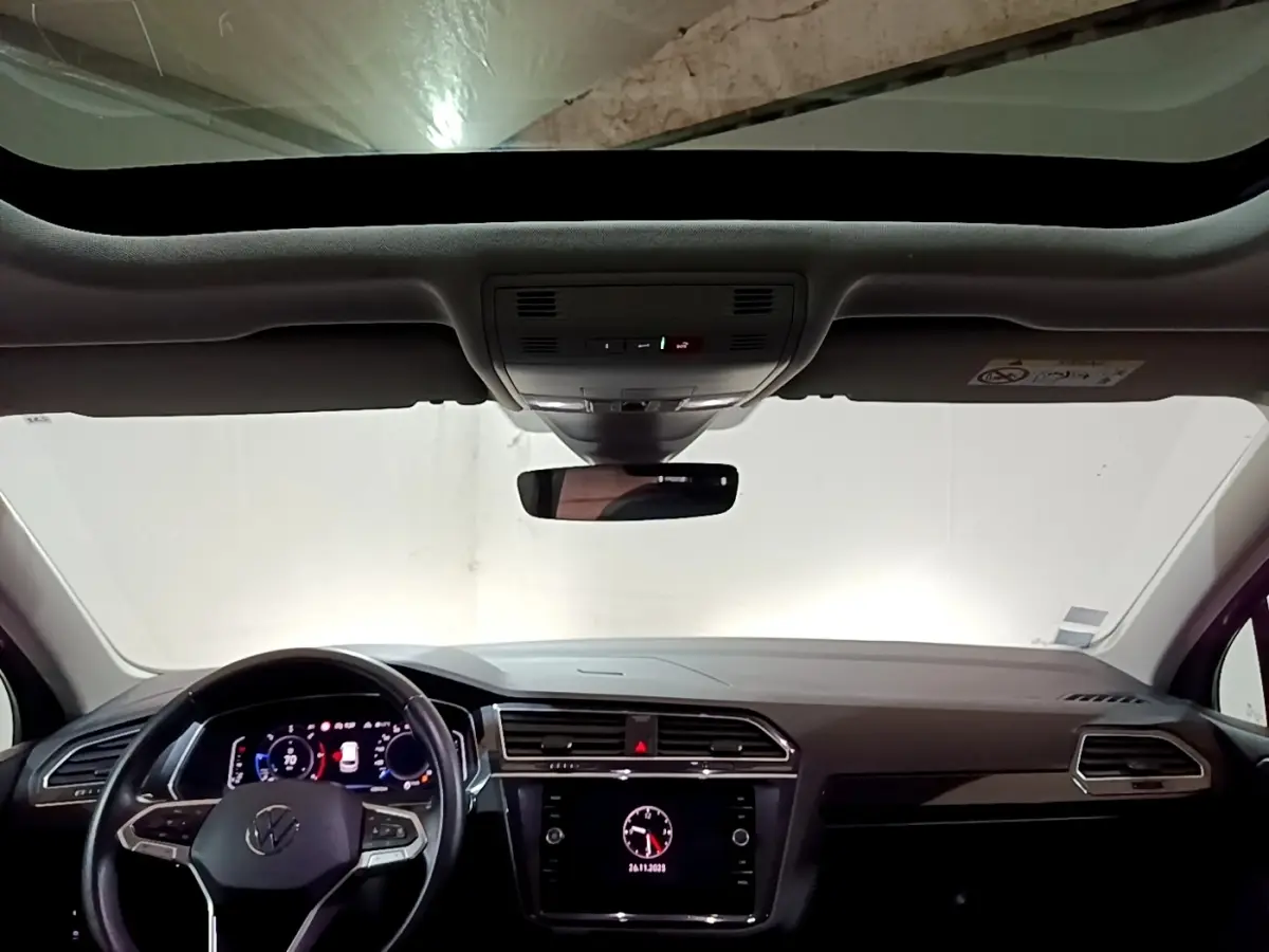 Vue intérieure avant du Volkswagen Tiguan 2.0 TDI gris foncé, tableau de bord moderne avec écran tactile et toit ouvrant panoramique.