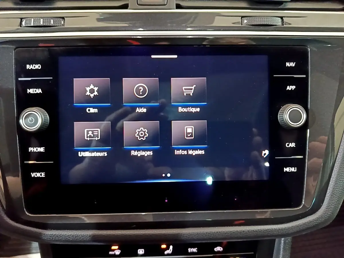Écran tactile central du Volkswagen Tiguan 2021 affichant les menus climatisation, aide et boutique, entouré de commandes noires.