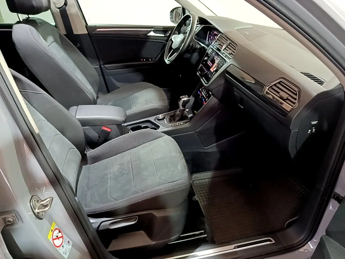 Intérieur avant du Volkswagen Tiguan gris foncé, montrant sièges tissu, volant cuir multifonctions et écran tactile central.