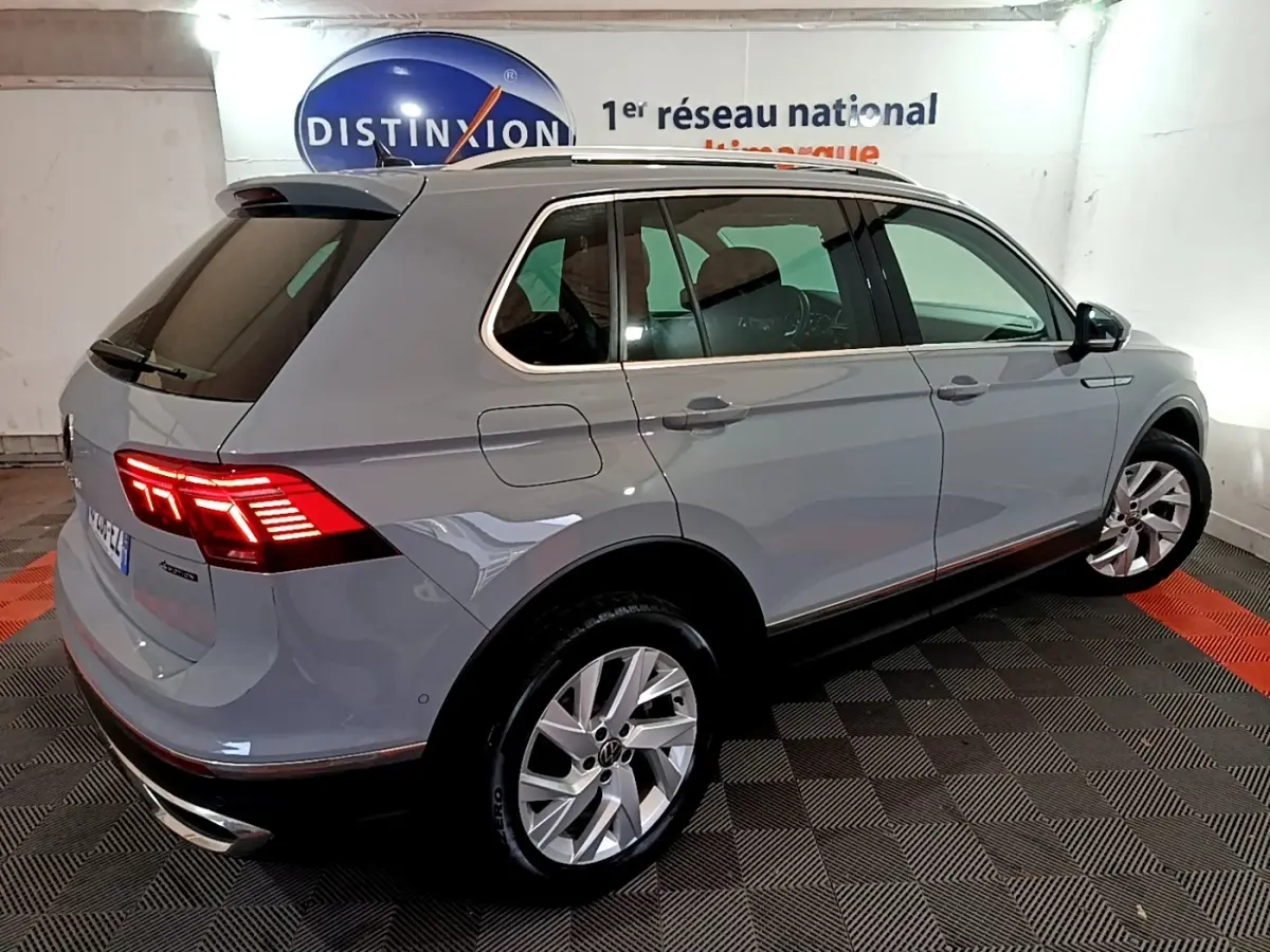 Volkswagen Tiguan gris foncé vu 3/4 arrière droit avec feux LED allumés dans un showroom intérieur.