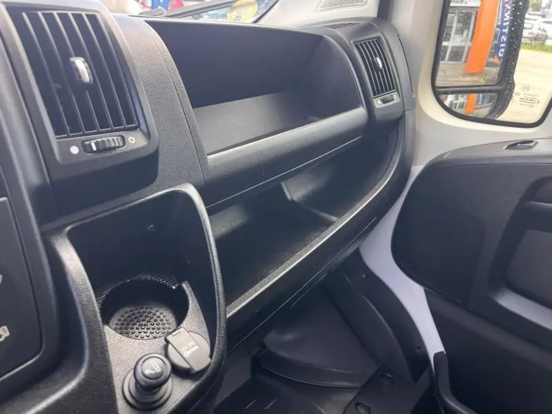 Vue intérieure côté passager du tableau de bord noir du Citroën Jumper blanc Icy avec rangements et prise 12V visible.