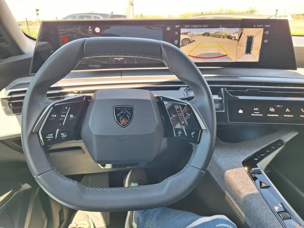 Vue intérieure centrée sur le volant cuir du Peugeot 3008 Hybrid 2025 avec cockpit numérique et écran d’aide au stationnement.