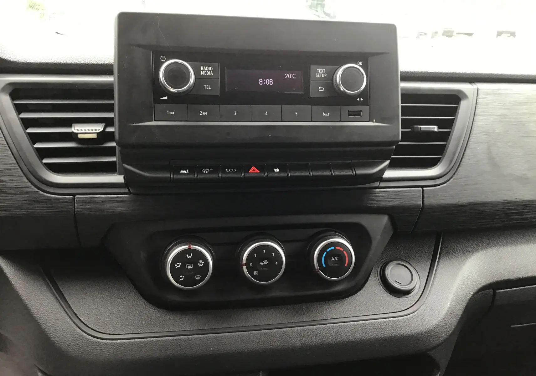 Vue rapprochée du tableau de bord noir avec radio et commandes de climatisation du Renault Trafic Fourgon blanc 2024.