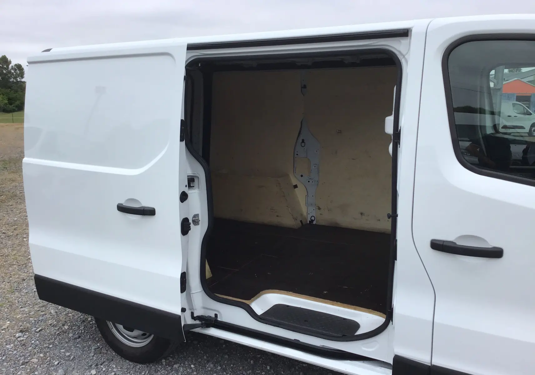 Vue latérale droite du Renault Trafic Fourgon blanc 2024 avec porte coulissante ouverte montrant l’espace de chargement vide.