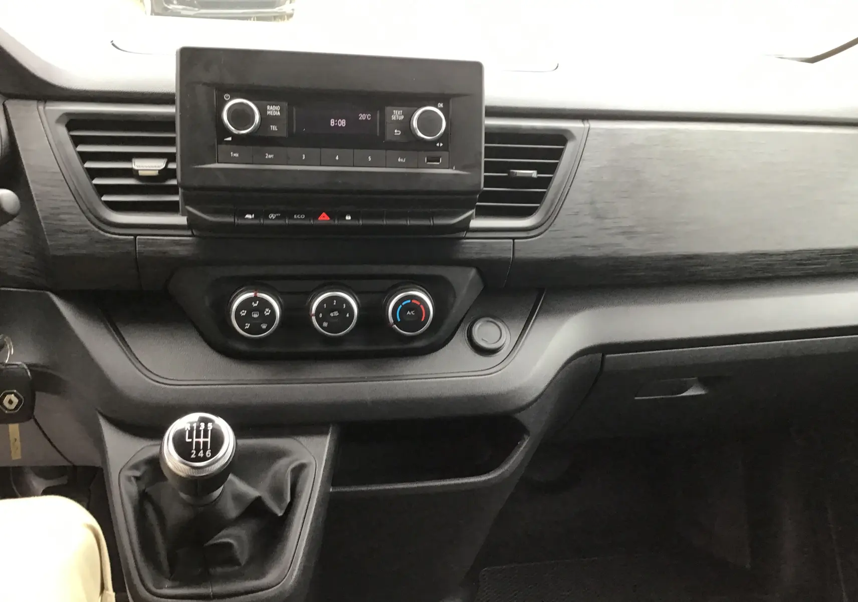 Tableau de bord du Renault Trafic Fourgon blanc 2024, vue intérieure centrée sur la console avec boîte manuelle et commandes clim.