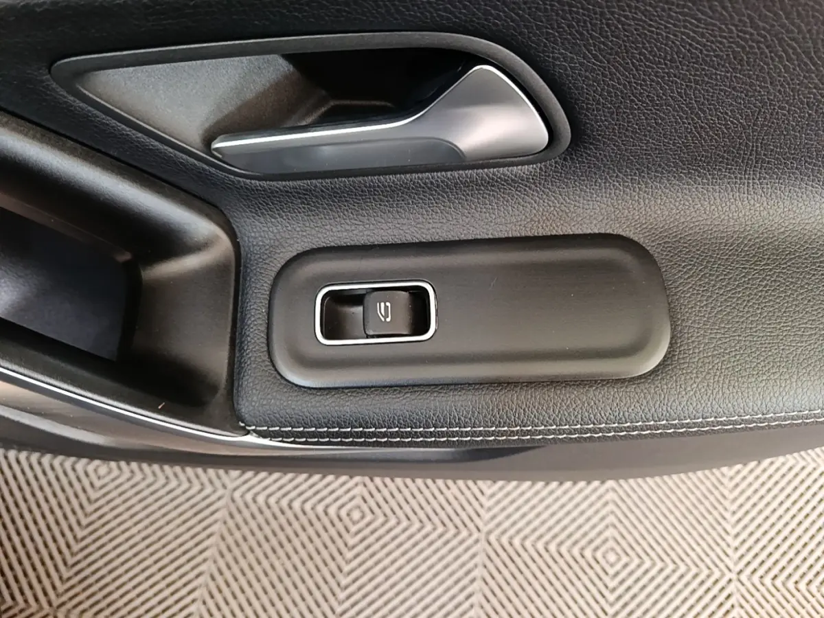 Gros plan sur la commande de lève-vitre côté conducteur en cuir noir avec surpiqûres blanches dans une Mercedes Classe A 2023.