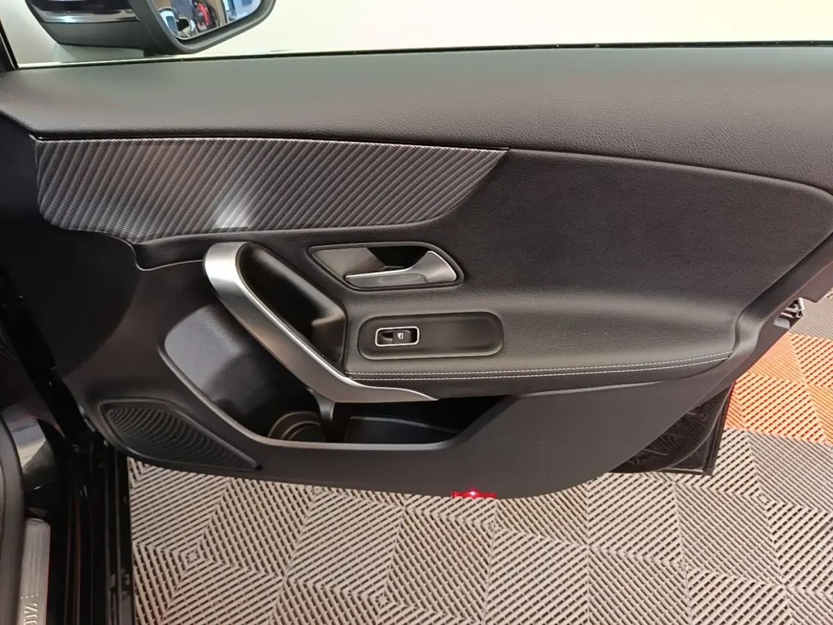 Vue rapprochée de la porte côté conducteur noire de la Mercedes Classe A 250 e Business Line 2023 avec insert carbone et poignée alu.