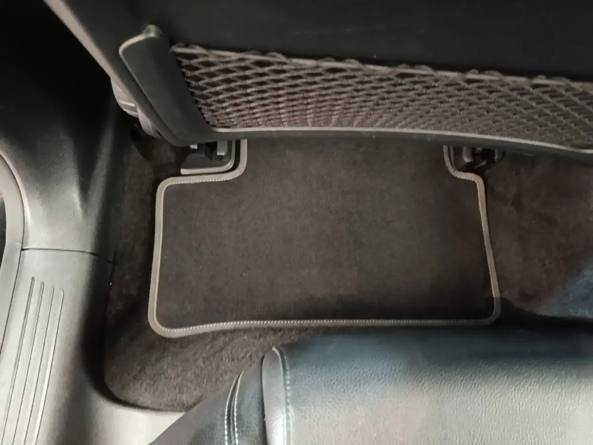 Détail du tapis de sol noir et du filet de rangement sous le siège arrière d'une Mercedes Classe A 250 e 2023.