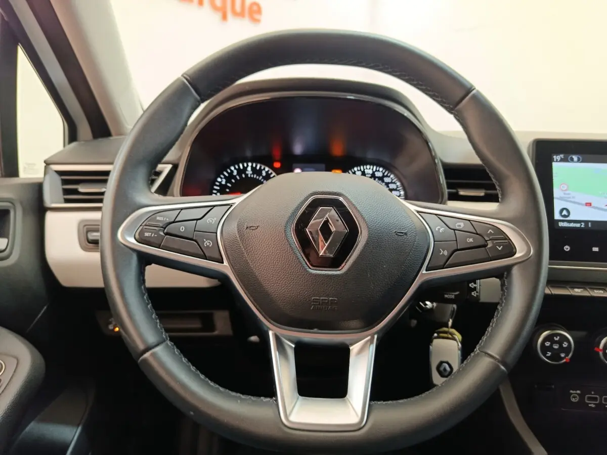 Vue rapprochée du volant en cuir synthétique noir de la Renault Clio 2023 avec tableau de bord et écran tactile visible.