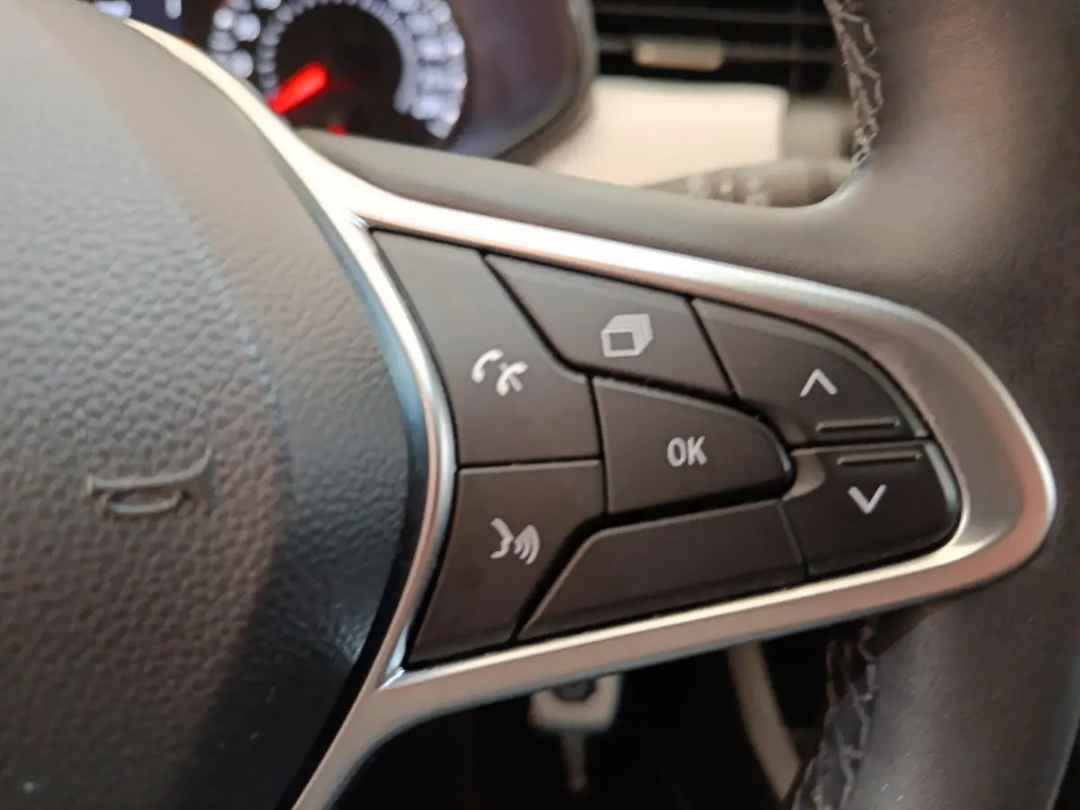 Gros plan sur les commandes multifonctions à droite du volant cuir synthétique de la Renault Clio blanche Evolution TCe 100 GPL 2023.