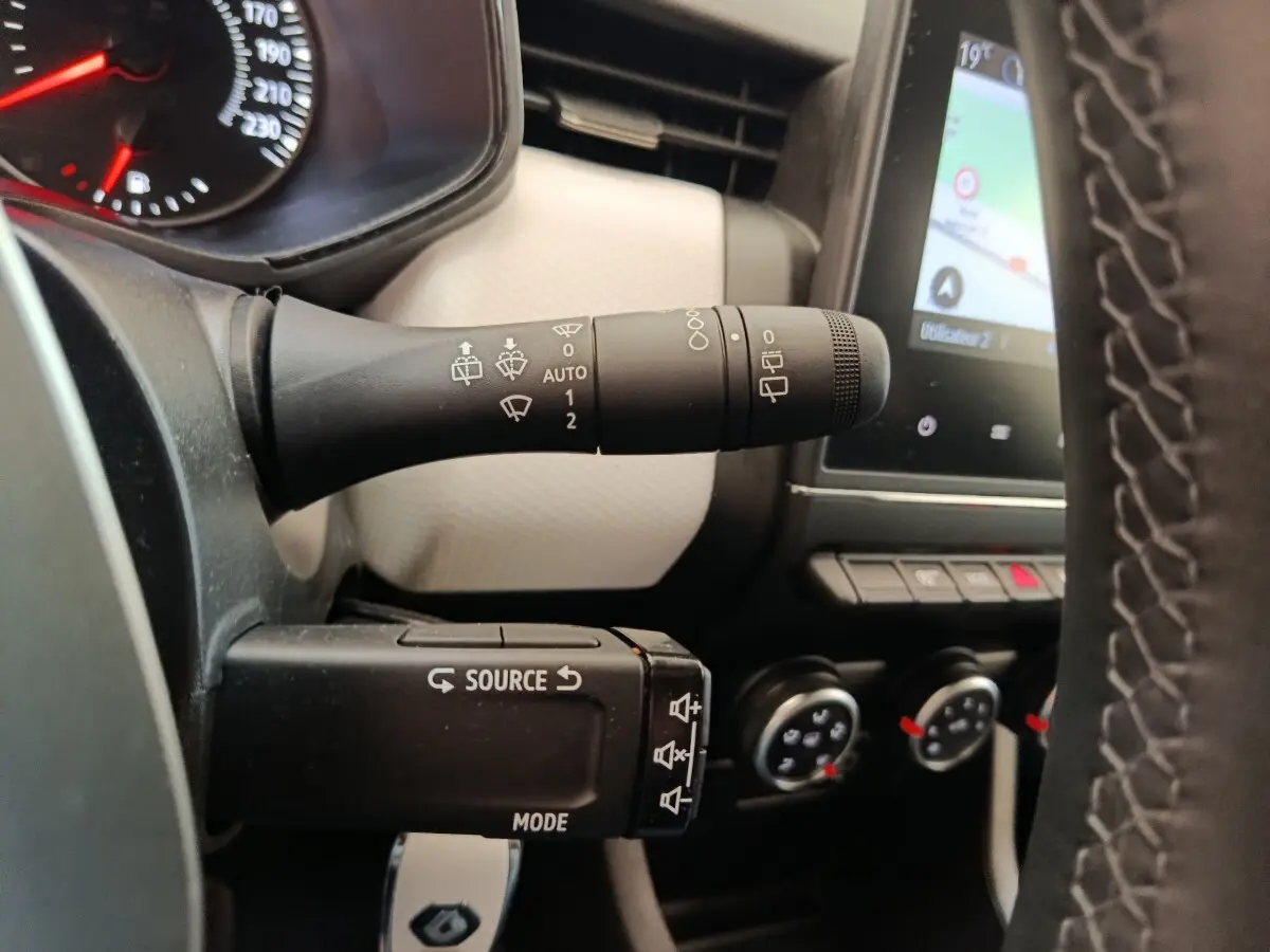 Gros plan sur la commande d’essuie-glace et le volant cuir synthétique de la Renault Clio blanche, avec écran tactile en arrière-plan.