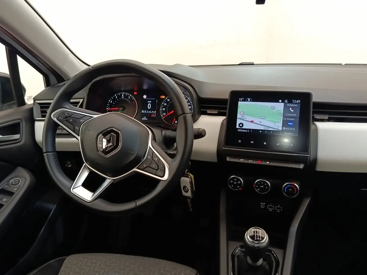Vue intérieure avant de la Renault Clio blanche 2023, volant multifonctions, écran tactile navigation et levier de vitesse manuel.