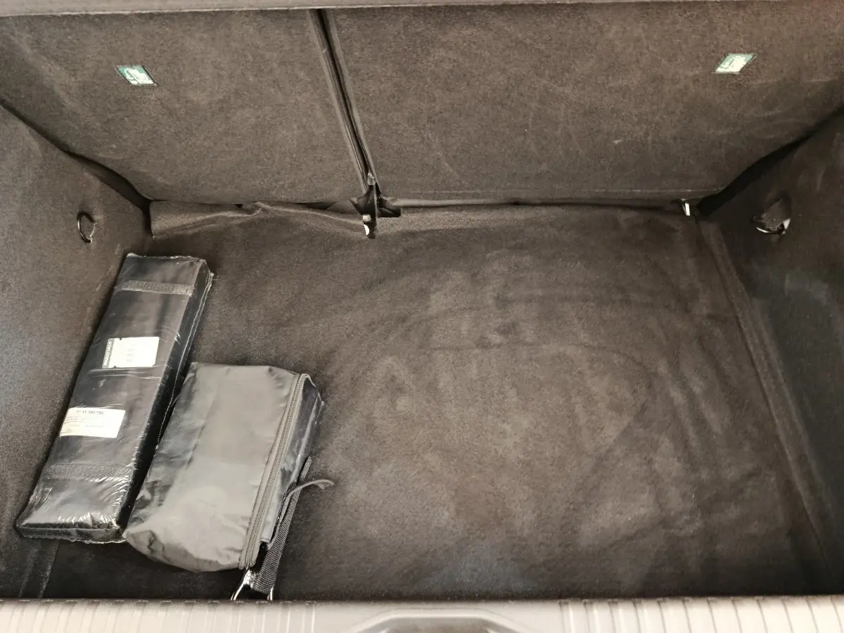 Coffre ouvert de Renault Clio blanc, vue intérieure montrant le tapis noir et deux sacs de rangement.