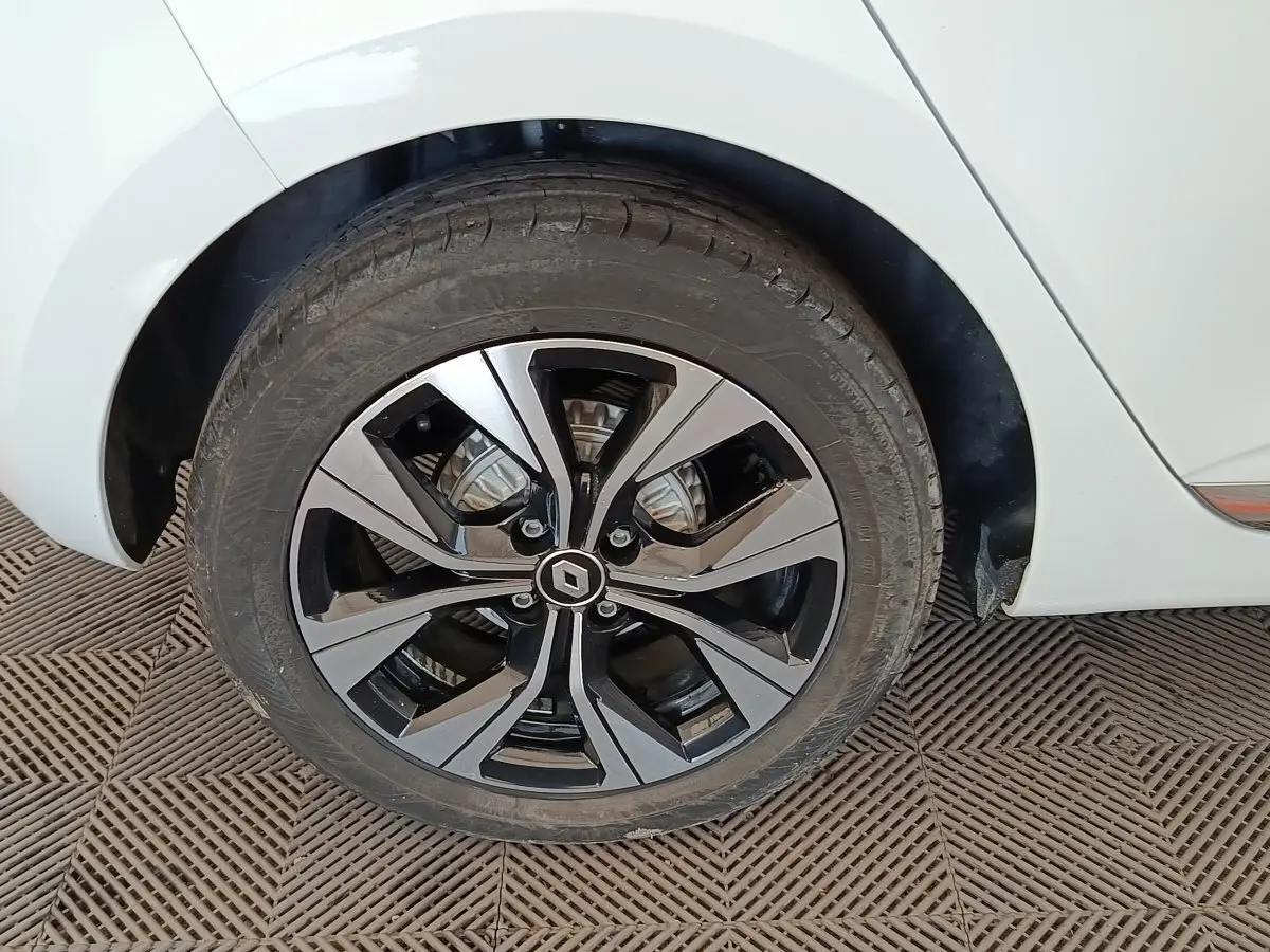 Gros plan sur la roue arrière droite d'une Renault Clio blanche avec jante alliage bicolore au design moderne.