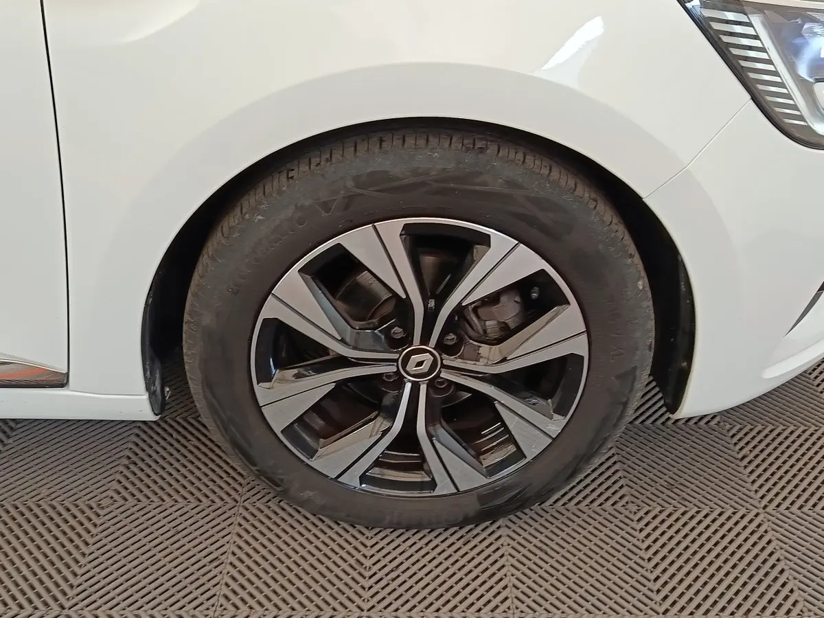 Gros plan sur la roue avant droite de la Renault Clio blanche, avec jante alliage bicolore et logo central Renault.