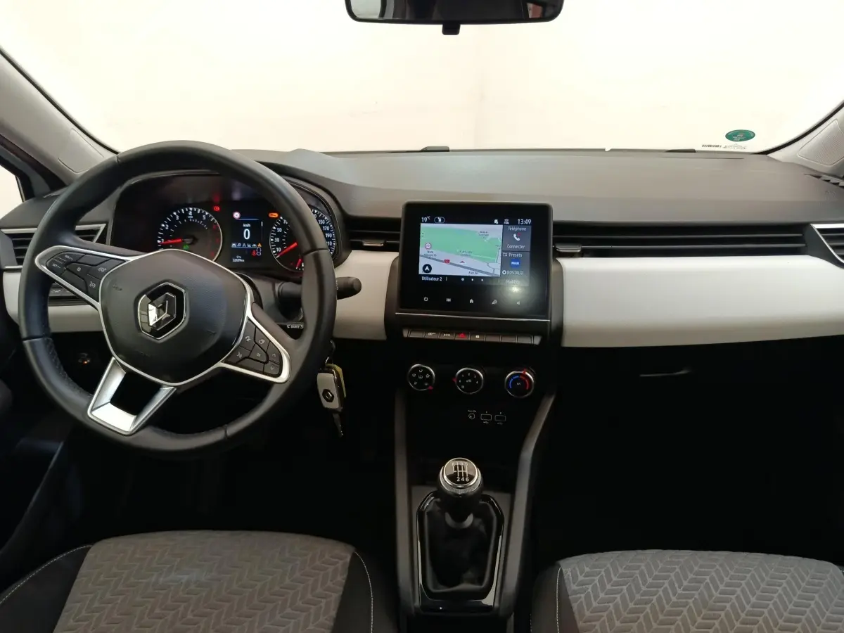 Vue intérieure avant de la Renault Clio blanche 2023 avec volant multifonctions, écran tactile central et boîte manuelle.