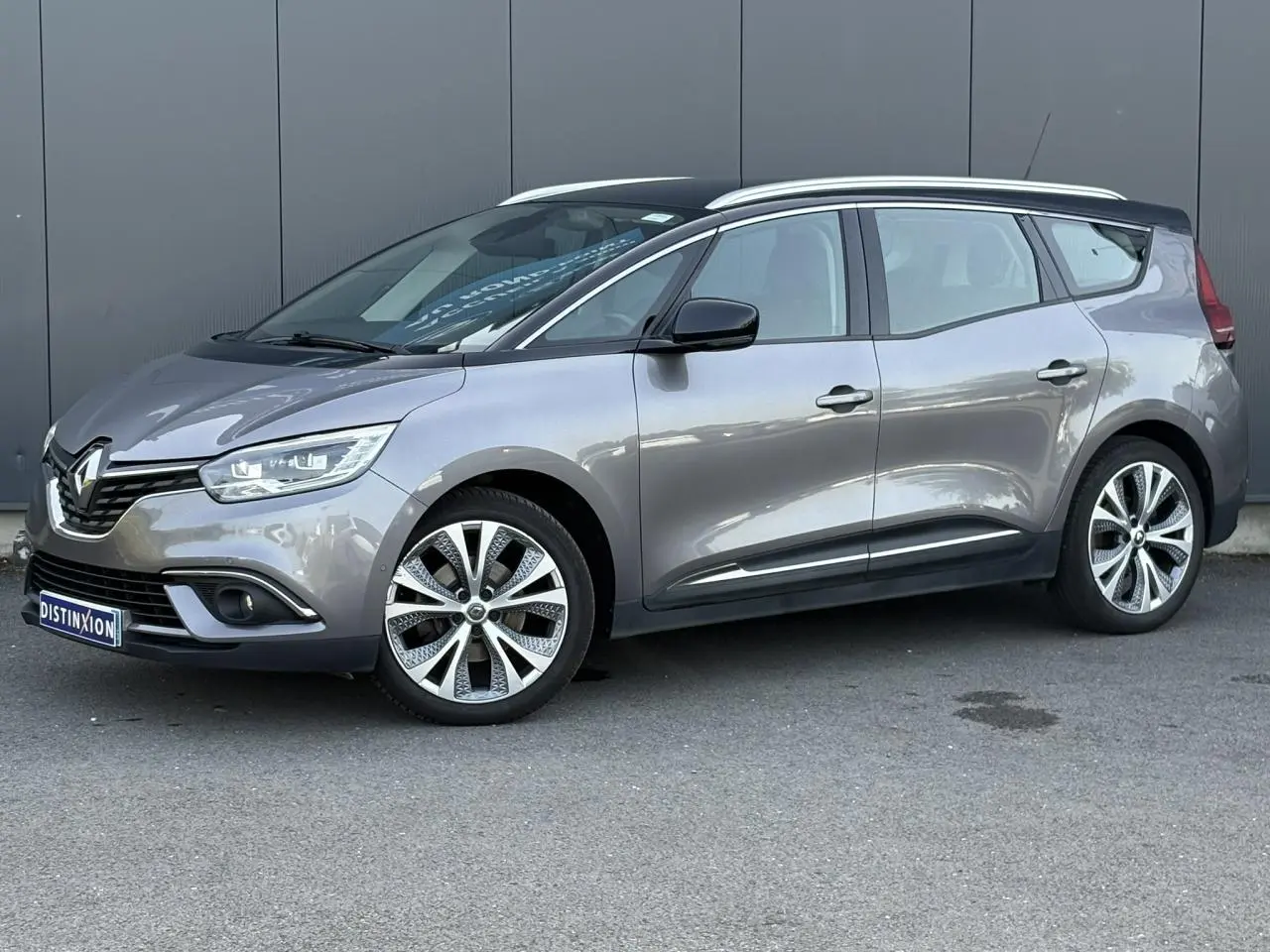 Renault Grand Scénic gris Cassiopée en vue 3/4 avant droit avec barres de toit chromées et jantes alliage 20 pouces.