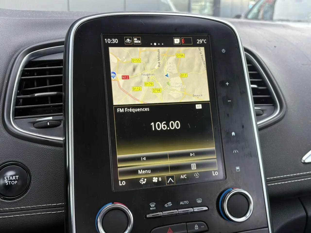 Écran tactile central du Renault Grand Scénic IV avec navigation et réglages climatisation, entouré d'aérateurs noirs.