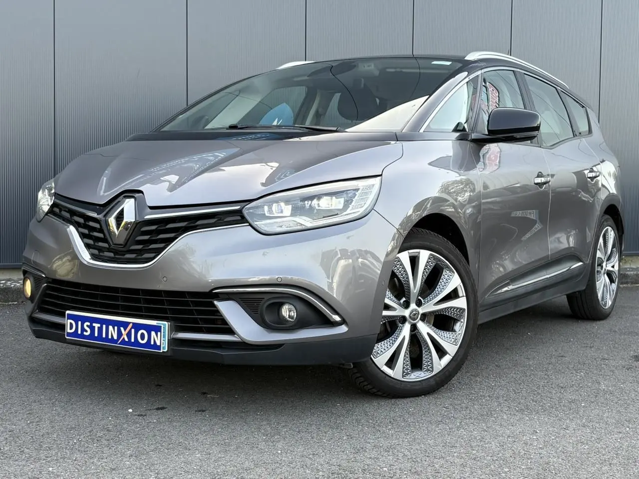 Renault Grand Scenic IV gris Cassiopée en 3/4 avant droit, avec jantes alliage 20 pouces et barres de toit chromées.